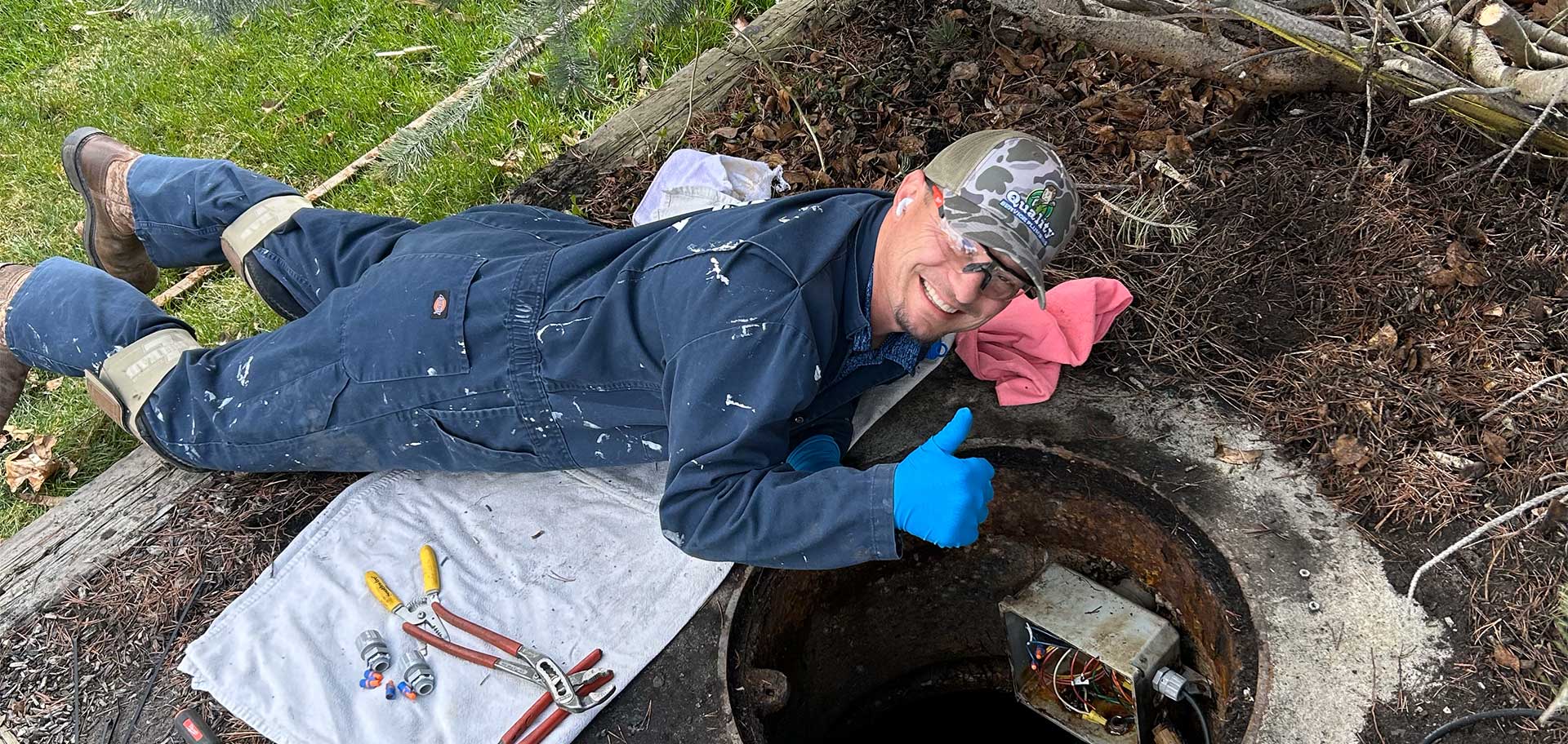 Plumber checking a sewer line, laying on the ground with a thumbs up.