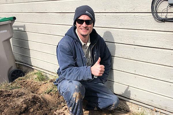 Plumbing technician next to a house with a thumbs up.