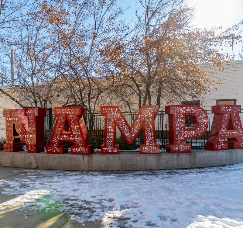 Nampa Idaho sign in red on a curved corner. The letters have words related to Nampa in them and the state of Idaho is on the lower part of the N.