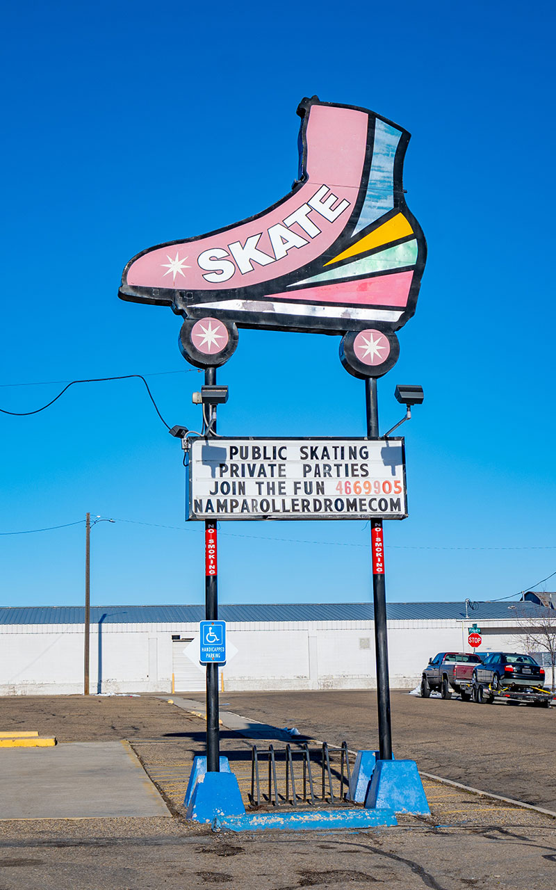 Nampa Idaho Roller Drome sign with a giant pink skate on top. The words skate in white on the large skate. Bright blue sky.