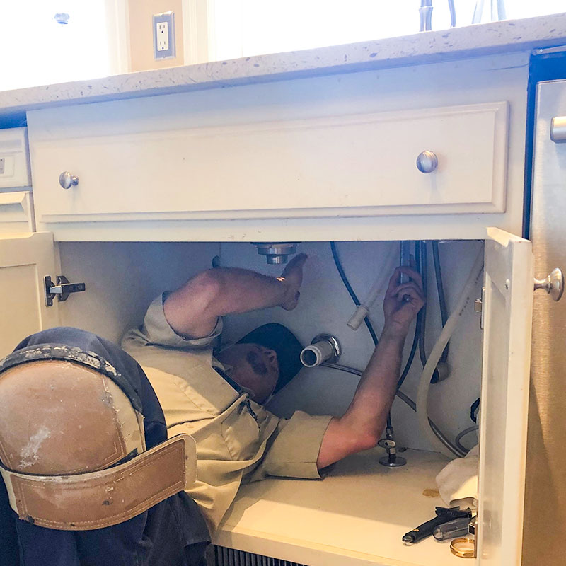 Plumber working under a kitchen sink.