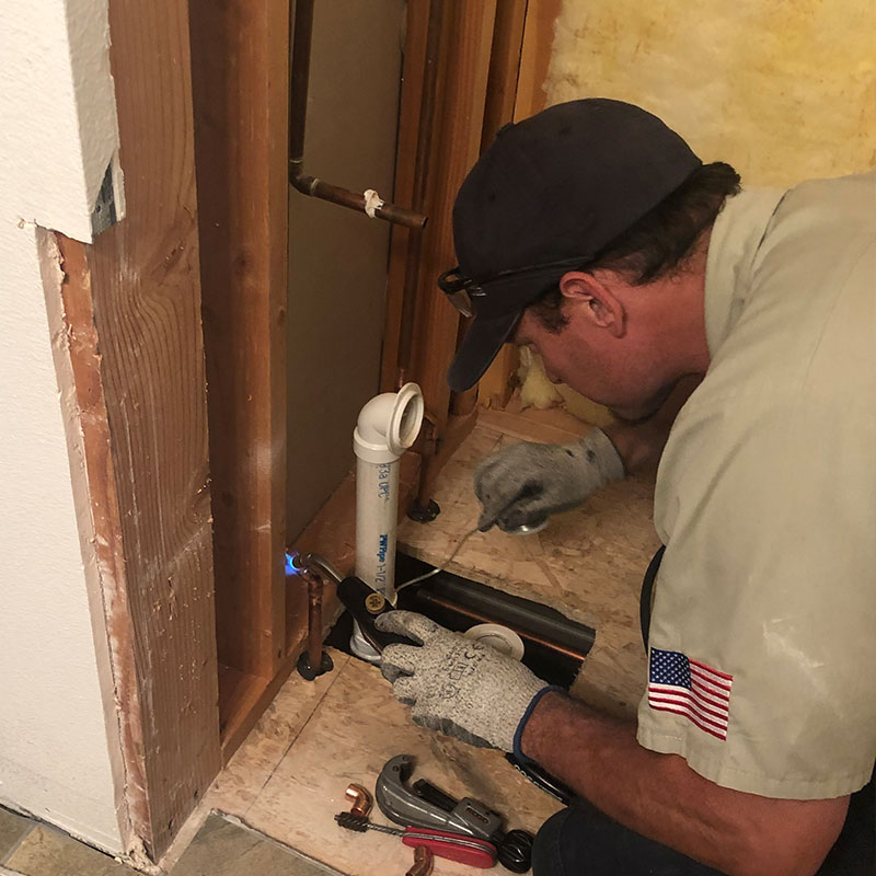 Plumber working on pipe coming out of flooring.