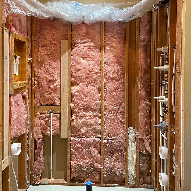 The rough in of a shower, the exposed walls have pink insulation and roughed in pipes.