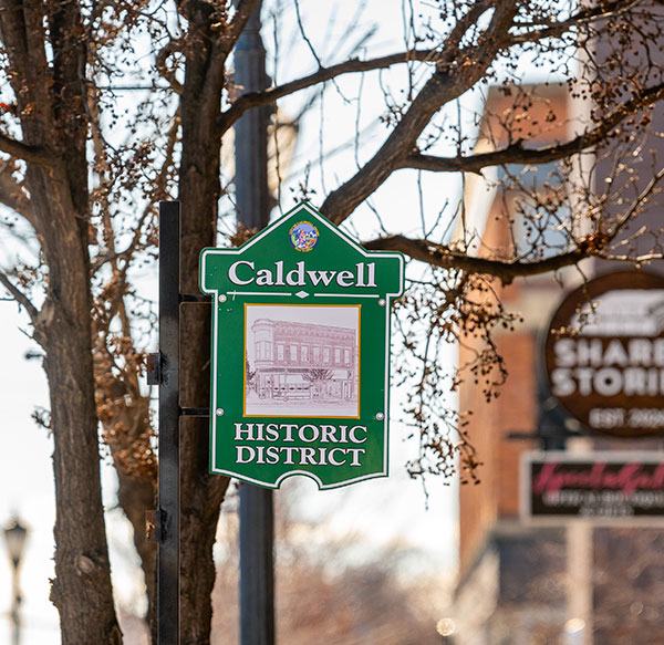 Downtown Caldwell Idaho sign. The sign is green with an illustration of old Caldwell on a green sign hung on a post.