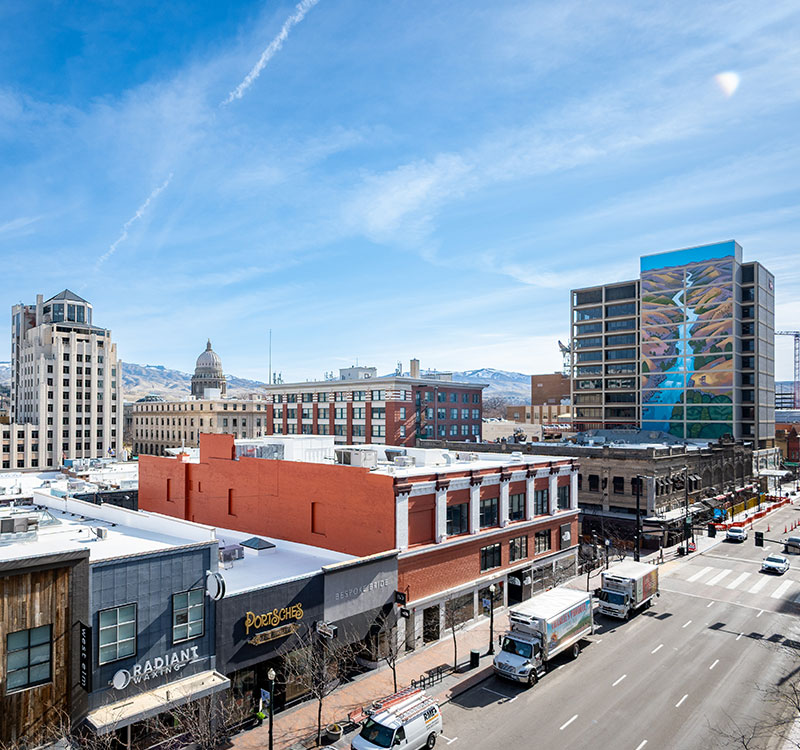 Downtown Boise with multiple buildings. The capital can be seen peaking out of the background. A building in the far right has a mural of a river.