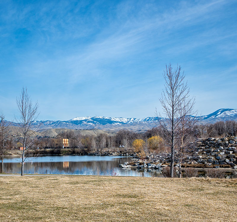 Park with a pond and rock feature. Snow capped mountains are seen in the background.