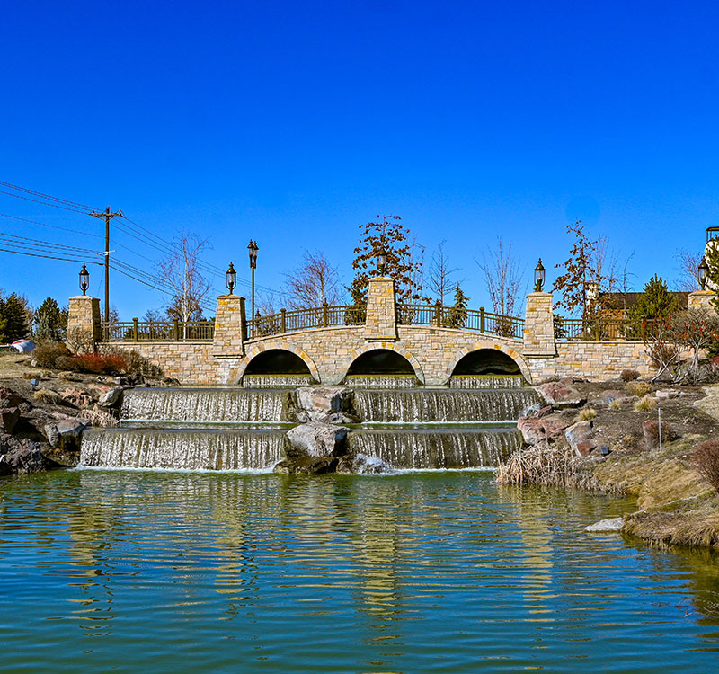 A bridge over a man made waterfall with a bright blue sky.