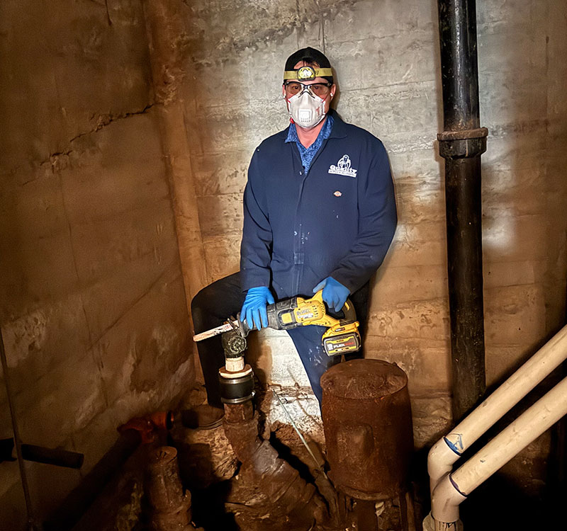 Plumber working in a basement on an old sump pump.