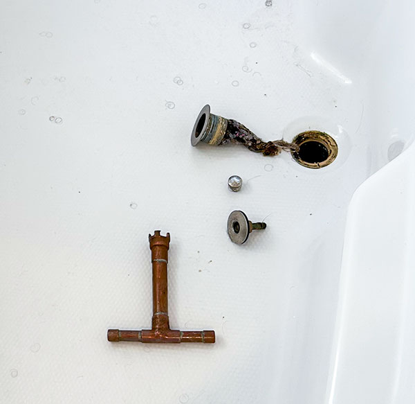 Bathtub with an exposed clogged drain with hair and plumbing tools.
