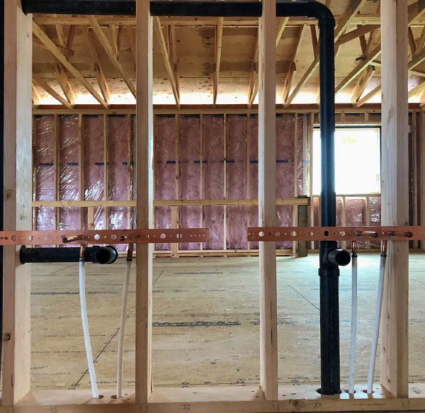 An exposed wall showing a black pipe going through the framing.