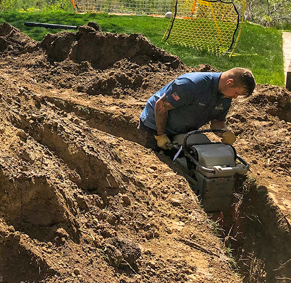 Plumbing technician with equipment helping to install a replacement sewer line in a dirt tunnel.