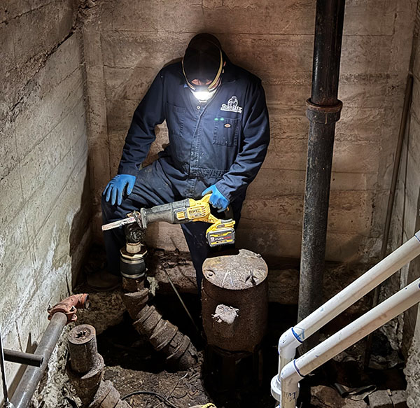 Quality Service Plumbing plumber working on a sump pump in a dark space.