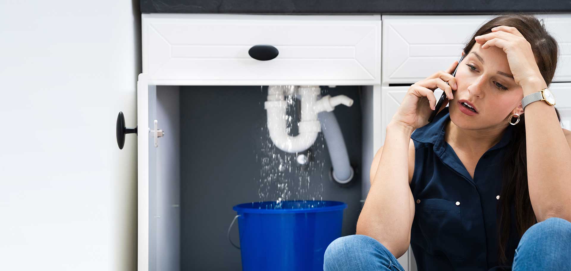 Woman on the phone stressed over a leak from under her sink.