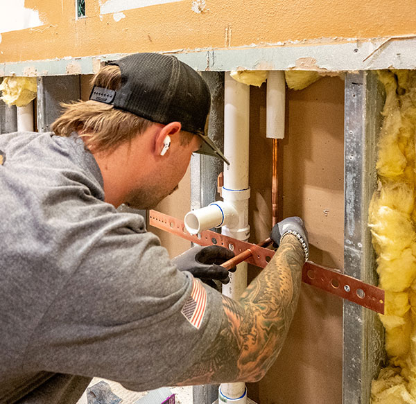 Plumber installing copper pipes in a wall.
