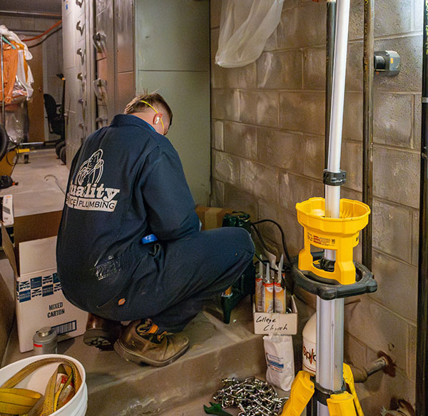 Plumbing technician crouched in a basement assembly some sewage parts.