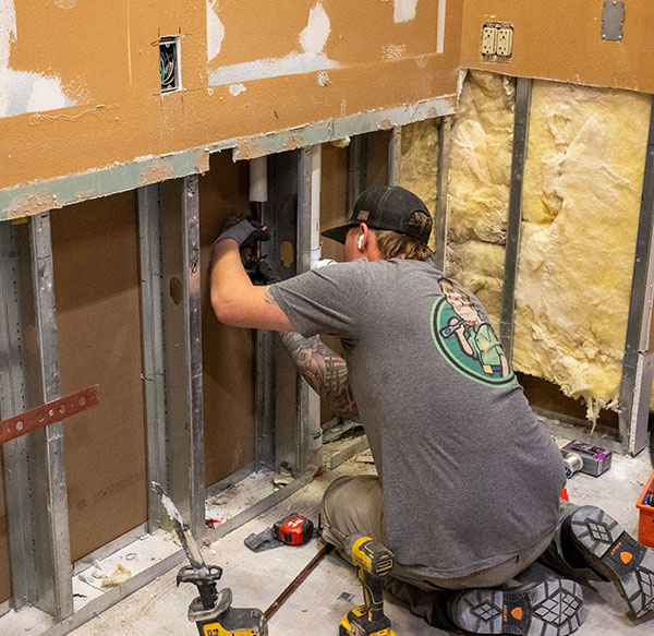 Plumber working on pipes in a remodel with exposes walls and piping.